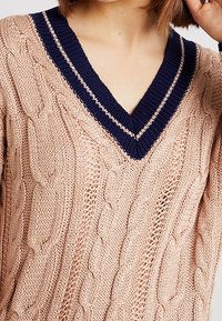 Maglione beige a maglia con scollo a V profondo in navy e strisce beige chiaro sul torso superiore di una persona.