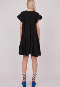 Robe noire à volants avec des manches courtes et froncées ; fabriquée dans un tissu léger ; présente une coupe décontractée et une longueur au-dessus des genoux.