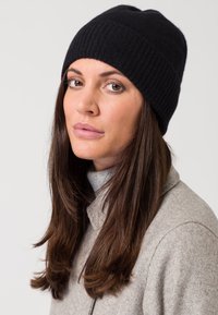 Gorro de punto negro con textura acanalada, que presenta un diseño ajustado. Se lleva con un abrigo de color gris claro con cuello y un cuello de tortuga.