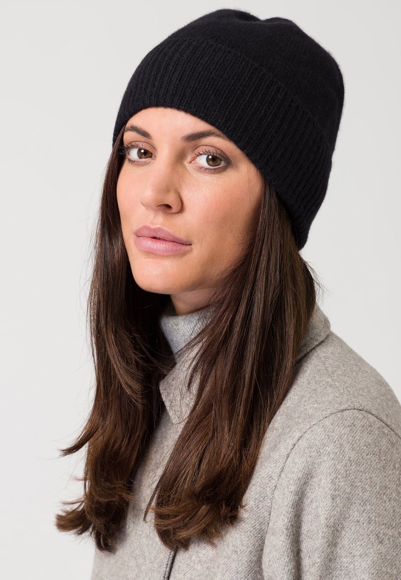 Gorro de punto negro con textura acanalada, que presenta un diseño ajustado. Se lleva con un abrigo de color gris claro con cuello y un cuello de tortuga.