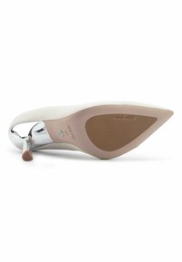 White patent leather high heel shoe with a pointed toe and a chrome accent on the heel. The sole is tan with ribbed texture and branding.