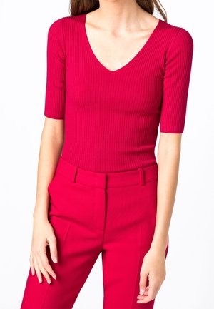 Getailleerde geribbelde top in felroze met een diepe V-hals en korte mouwen, gecombineerd met bijpassende hoge taille broek. Soepele textuur, zonder versieringen.