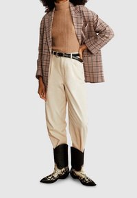 Karierter übergroßer Blazer, ribbed brauner Rollkragenpullover, beige weite Hose und schwarze Cowboy-Stiefel mit weißen Details. Texturierte Stoffe und Muster.
