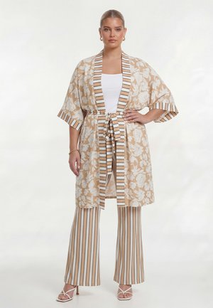 Kvinde iført beige kimono-stil jakke med blomstermønster og striped kant samt matchende striped vidde bukser, kombineret med hvid top og sandaler.