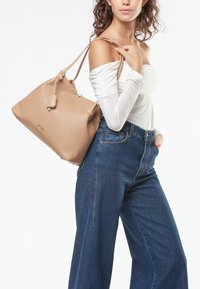 Borsa tote in pelle beige con doppi manici, una forma strutturata e un'etichetta piccola. Indossata con jeans in denim blu a vita alta.