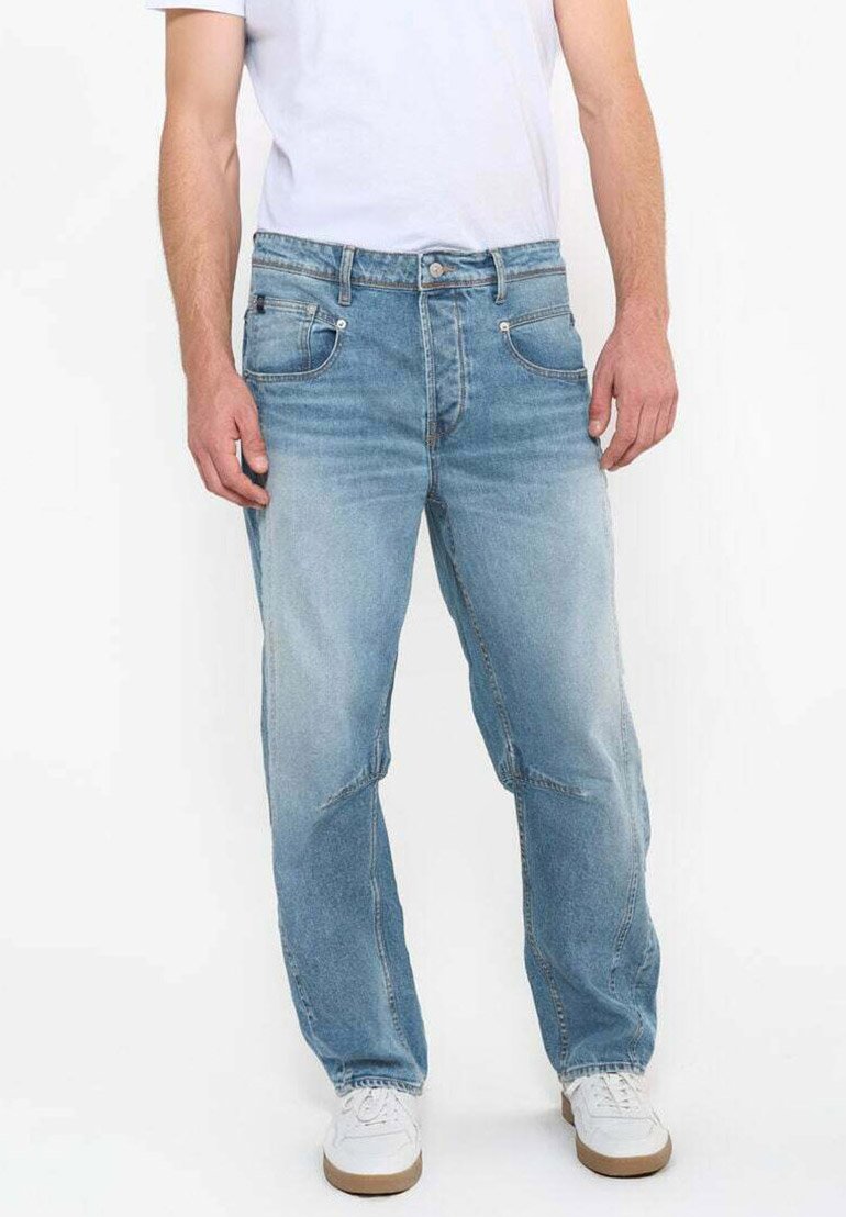 Jean en denim bleu clair délavé avec une coupe relaxed, cinq poches et de subtils détails de couture, porté avec un t-shirt blanc et des baskets blanches.