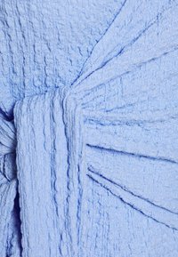 Ljusblått texturerat tyg med en skrynklig yta, med en knuten midja och draperade designelement. Inga synliga detaljer eller mönster.