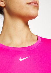 Aansluitend roze sportshirt, zachte stof, ronde halslijn, met een klein wit Nike-logo op de borst.