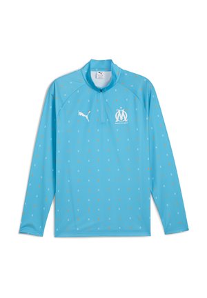 Lysblå langærmet pullover med lynlås ved halsen, prikket mønster i gult og hvidt, Puma-logo og holdemblem på brystet.