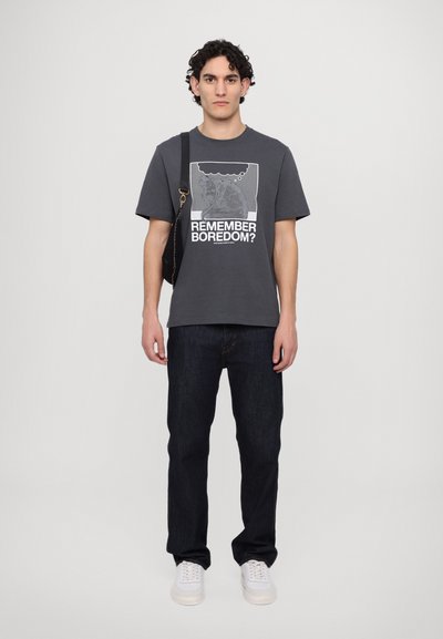 Gray graphic t-shirt with "REMEMBER BOREDOM?" text, worn with dark denim jeans and white sneakers. Features a relaxed fit and short sleeves.