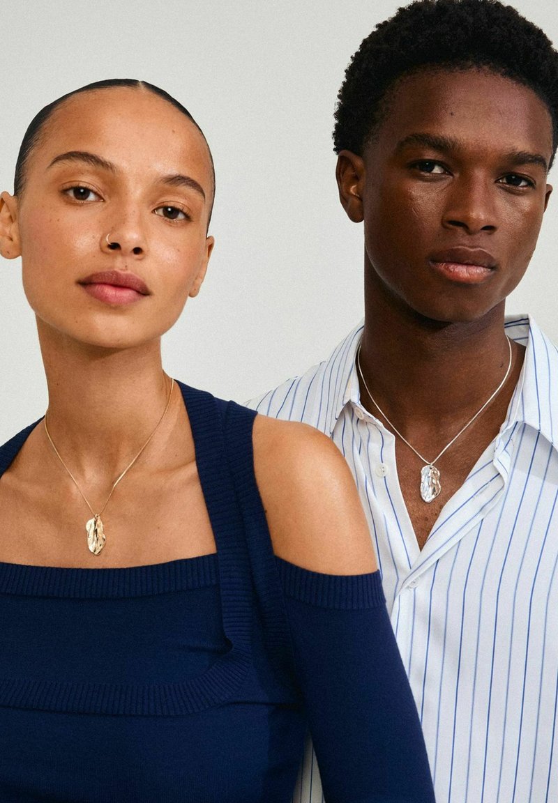 Top off-shoulder bleu marine et chemise rayée blanche, toutes deux ornées de colliers en pendentif argenté ; textures lisses et lignes épurées définies.