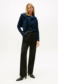 Cárdigan azul marino con cuello de chal, pantalones negros de cintura alta y tacones negros puntiagudos. Tejido texturizado en el cárdigan, tela suave en los pantalones.