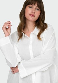 Camicia bianca a maniche lunghe con bottoni, realizzata in tessuto leggero con una vestibilità comoda e colletto classico. Presenta polsini arrotolati e bottoni a vista.