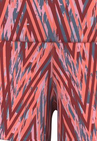 Flerfärgade mönstrade shorts i nyanser av röd, rosa och blå, med en zigzag-design och ett mjukt, stretchigt material. Sömmarna är synliga.