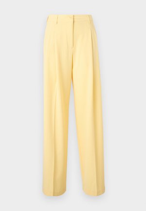 Pantalon jaune taille haute à jambes larges avec plis devant, passants pour ceinture et fermeture par bouton à la taille sur fond uni.
