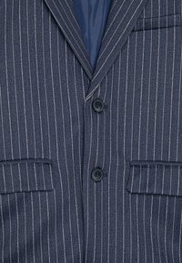 Granatowy blazer w paski wykonany z teksturowanej tkaniny. Posiada dwa czarne guziki, klapy z wycięciem oraz kieszeń na lewym udzie.