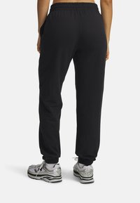 Pantaloni della tuta neri con vita e polsini elastici, dotati di tasche laterali. Abbinati a scarpe da ginnastica argento e grigie.