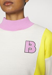 Pull avec un col côtelé rose, un corps blanc et des manches jaunes, affichant un logo "BOSS" rose bien en vue sur la poitrine.