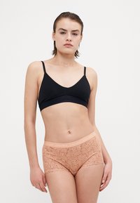 Fekete, varrás nélküli bralette vékony pántokkal; bézs mintázatú hipster alsóneművel párosítva, díszes mintázattal és logózott derékrésszel.
