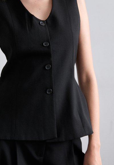 Svart ermeløs topp med v-hals, fem svarte knapper foran og en strukturert peplum-design. Glatt stoff med en matt finish.