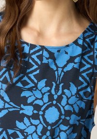 Haut à imprimé floral bleu avec un col rond, présentant un fond contrastant en navy et un tissu texturé.