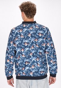 Giacca bomber navy con un vivace motivo floreale che presenta foglie tropicali e fiori di uccello del paradiso arancioni. Polsini e orlo a coste.