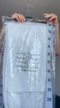 Vesel alb pe un umeraș negru, ambalat în plastic, cu eticheta de mărime "38" vizibilă. Textul de pe ambalaj include instrucțiuni de îngrijire și avertismente.