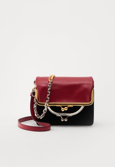 Sac à main en cuir rouge et noir avec des accessoires en or, bandoulière en chaîne et détails de fermoir, forme rectangulaire, surfaces lisses et texturées.