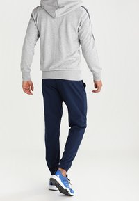 Sudadera gris con cremallera y capucha, pantalones joggers azul marino y zapatillas deportivas azules. Los pantalones tienen una cintura elástica y puños ajustados.