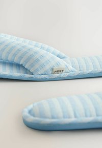 Blå og hvide stribede tekstilslippers med en quiltet design. De har en rund tå og et lille mærke med teksten "NEXT" på siden.