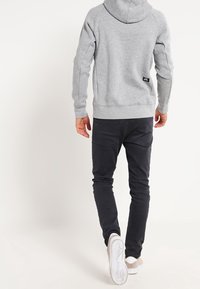 Sudadera gris con capucha, puños y dobladillo acanalados. Combinada con jeans oscuros y zapatillas claras. Diseño simple, sin patrones ni adornos.