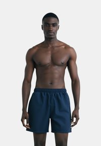 Pantaloni da nuoto blu navy realizzati in tessuto leggero con cintura elastica e strisce laterali. Presentano un taglio dritto e una texture morbida.