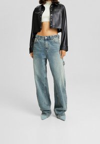 Czarna kurtka z sztucznej skóry o kroju cropped z srebnymi dodatkami, zestawiona z jasnoniebieskimi spodniami o szerokich nogawkach i spiczastymi, jasnoniebieskimi szpilkami.