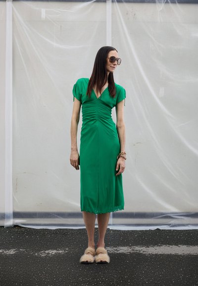 Zelené midi šaty s krátkými balónovými rukávy, nařasené v pase a vroubkovaným lemem, doplněné chlupatými nazouváky.