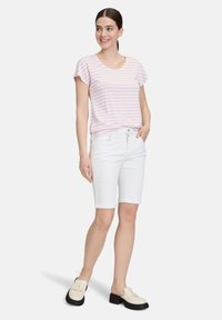 Różowo-biały, pasiasty t-shirt z krótkim rękawem połączony z białymi dżinsowymi szortami z podwiniętymi nogawkami. Model nosi jasne buty wsuwane z grubą podeszwą.