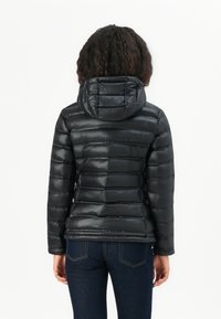 Čierna puffa bunda s horizontálnym prešívaním, obsahuje kapucňu a hladký, lesklý povrch. Nosená s tmavými džínsami.