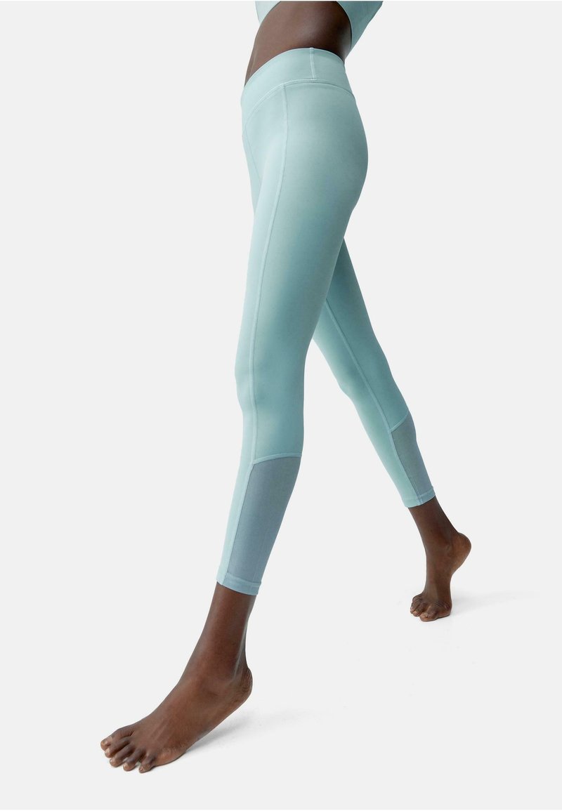 Leggings azzurri chiari realizzati in un tessuto morbido e elasticizzato. Presentano un vita media e un pannello grigio a contrasto nella parte inferiore della gamba.