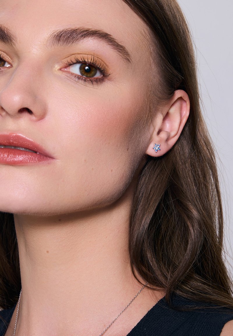 Niebieska, gwiazdkowa kolczyk z kamieniem szlachetnym, osadzony w metalowej oprawie. Zbliżenie ukazujące kolor i design kolczyka na neutralnym tle.