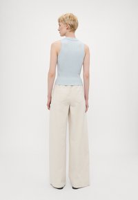 Top senza maniche a costine blu chiaro abbinato a pantaloni beige a vita alta e a gamba larga, che mostrano una texture morbida e una vestibilità rilassata.