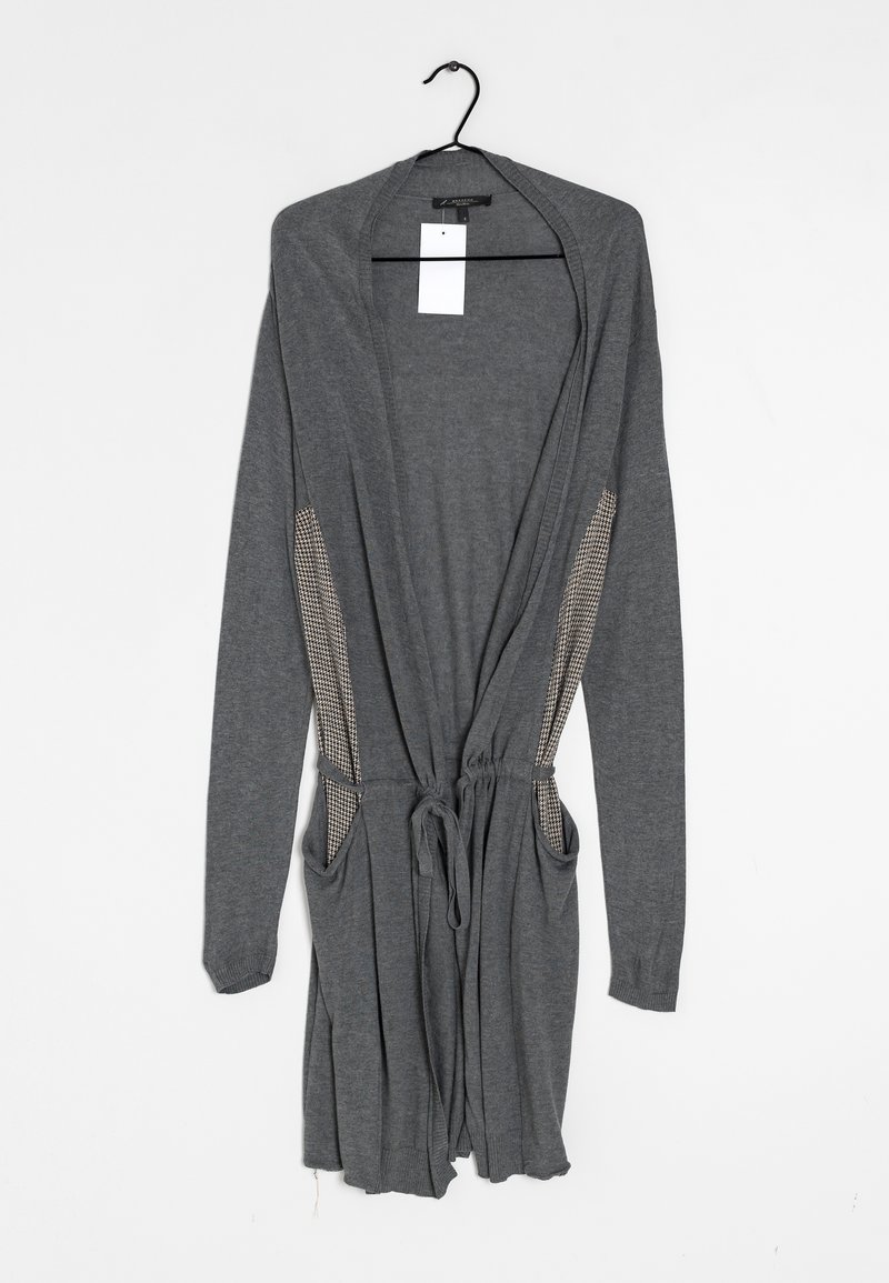 Cardigan gris à manches longues avec ouverture sur le devant, ceinture à cordon, panneaux latéraux à carreaux et poches avant, suspendu sur un cintre noir.