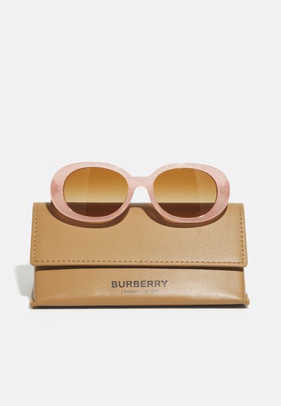 Lunettes de soleil Burberry avec une monture rose mate et des verres dégradés marron, posées sur une pochette en cuir beige avec une marque visible.