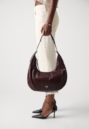 Purple leather hobo bag with a matte finish, softly rounded shape, and metal logo detail. Paired with white jeans and black heels.