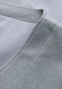 Szara, teksturowana tkanina z gładkimi, jasnoszarymi sekcjami. Posiada czysty szew i zaokrąglony brzeg, podkreślając kontrast w materiale i wykończeniu.