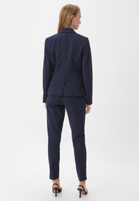 Marineblauw pak met een getailleerde blazer met één split en slim-fit broeken. Het materiaal is glad met een matte afwerking.