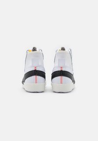 Höga sneakers med ett ovandel i vitt tyg, svarta läderdetaljer, röda sömmar och en texturerad gummisula. Minimalistisk design.