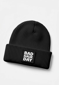 Black ribbed beanie made of soft fabric, featuring a rectangular patch with the text "BAD HAIR DAY" in white, prominent on the cuff.