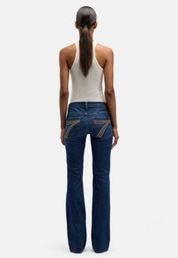 Figursydda jeans med blå tvätt och utsvängda ben, med unika sydda bakfickor och midjehöjd i midjan. Bomullsmaterial med lätt stretch.