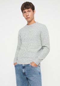 Gray cable-knit sweater with a round neckline, long sleeves, and a soft texture, paired with light blue jeans.