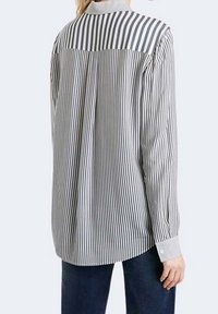 Camicia a righe grigia e bianca, con colletto, maniche lunghe e polsini con bottoni. Il materiale è leggero e ha una texture liscia.