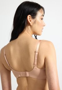 Ελαφρύ μπεζ σουτιέν με ρυθμιζόμενες τιράντες, ομαλή υφή και κλείσιμο με τρεις γάντζους στο πίσω μέρος. Απλός σχεδιασμός χωρίς διακοσμητικά.